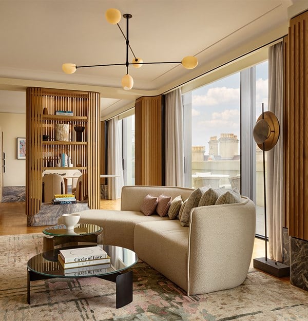 A bright suite living room with a curved cream sofa, glass coffee tables, and floor-to-ceiling windows opening to a terrace.