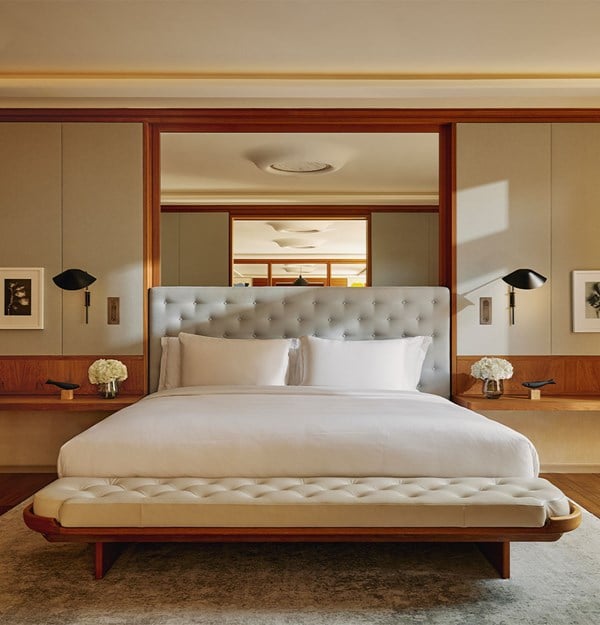 A modern suite bedroom with a tufted headboard, crisp white bedding, and warm wood panel accents.