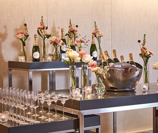 Champagne in ice buckets, champagne glasses and flower on high tables.