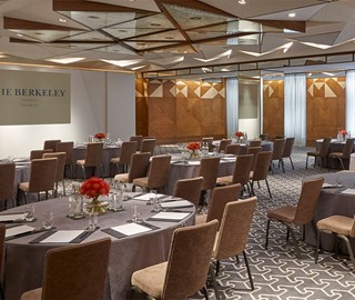 Room set up for a meeting with several round tables, papers, pens, glasses of water. At the back are two screens displaying 'The Berkeley' logo.