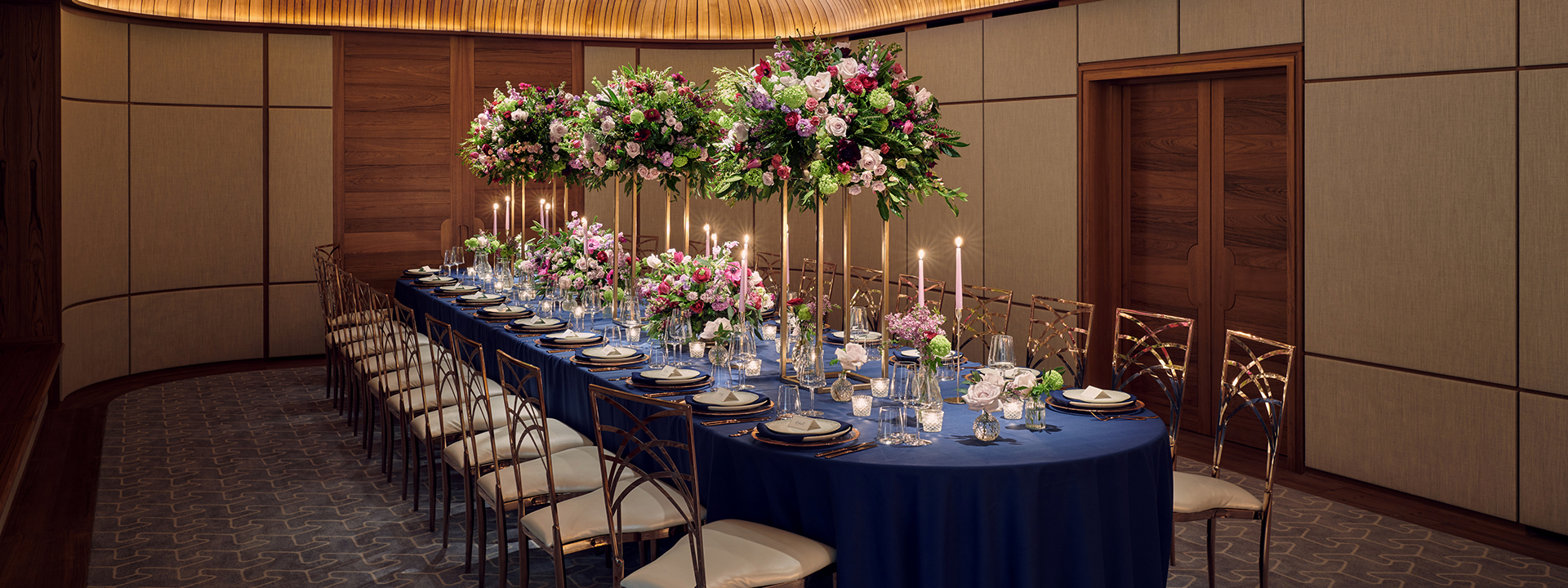 A richly decorated table with flowers and candles, on a blue tablecloth with golden chairs in The Wilton Room.