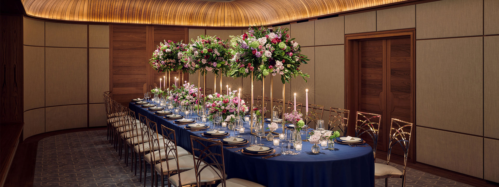 A richly decorated table with flowers and candles, on a blue tablecloth with golden chairs in The Wilton Room.