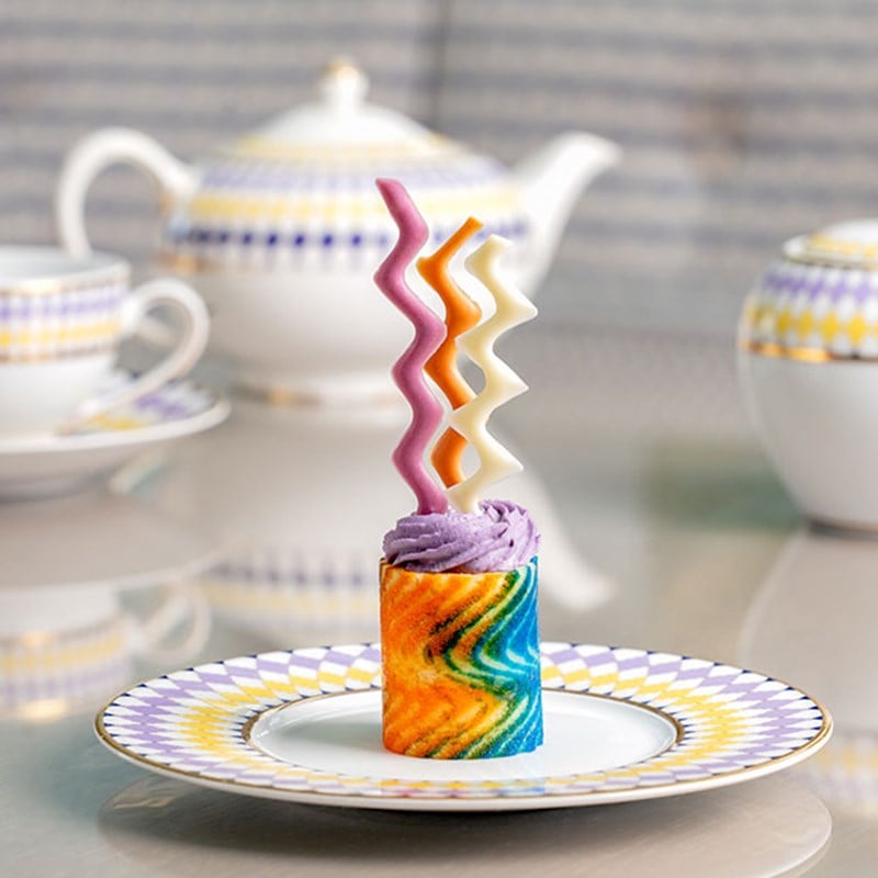 Rainbow coloured cake with swirl decoration on top on a plate