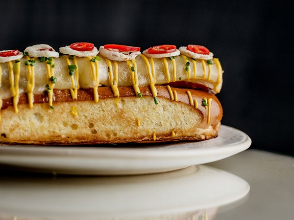 Close up of a hot dog with yellow sauce, chives and melted cheese on the top