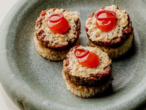 Steak tartare on bite-sized crumpets on a grey plate as bar snacks