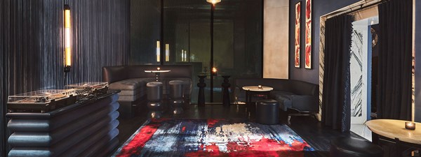 Inside of the glass pavilion of the Blue Bar with a red and blue abstract rug, a DJ decks and low blue bar stools