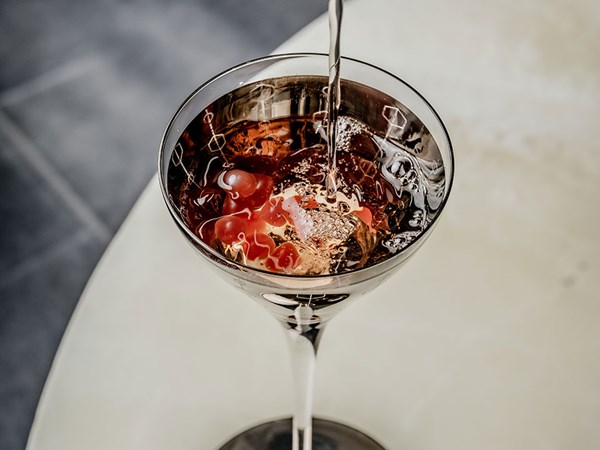 Red coloured cocktail being poured into a martini glass
