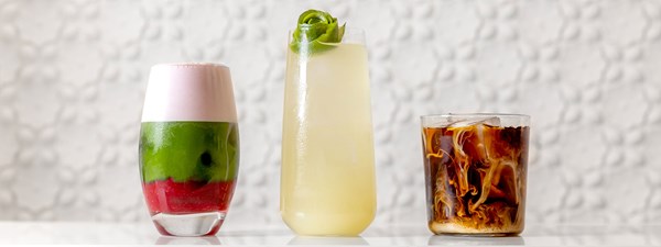 Three iced drinks lined up on the counter including a juice, an iced coffee and a layered ice drink