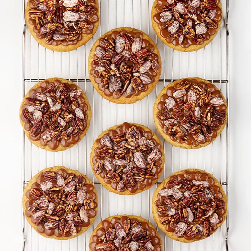 A tray of pecan tarts topped with glossy caramel and clusters of glazed pecans.