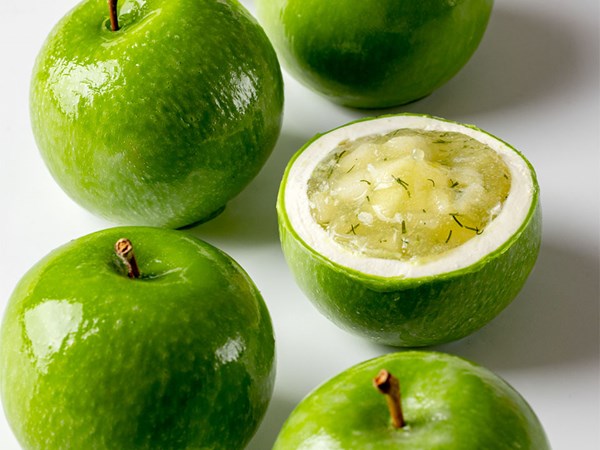 Glossy green apples, with one cut open to reveal a creamy white filling topped with translucent apple jelly and herb flecks.