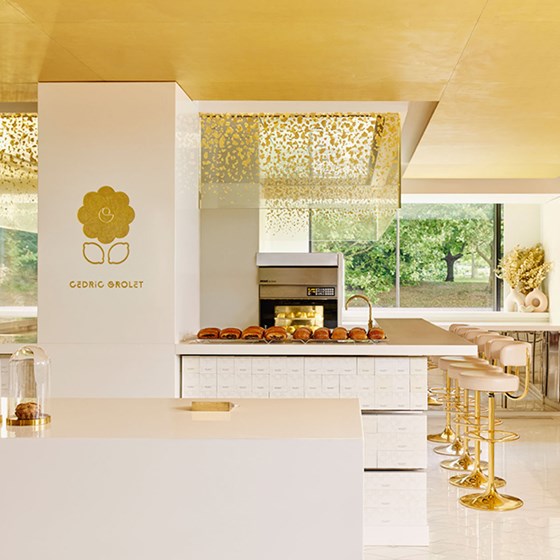 A luminous pâtisserie counter at Cedric Grolet at The Berkeley, with golden stools, pristine white surfaces, and a delicate display of viennoiserie beneath a gold-speckled canopy.