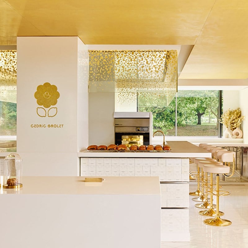 A luminous pâtisserie counter at Cedric Grolet at The Berkeley, with golden stools, pristine white surfaces, and a delicate display of viennoiserie beneath a gold-speckled canopy.