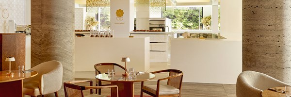 A wider view blending the serene café setting with Cedric Grolet’s minimalist pâtisserie, where curved seating and pale wood tones contrast beautifully with polished stone columns.