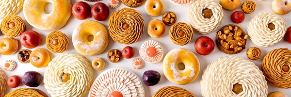 Panoramic arrangement of Cedric Grolet pastries in various shapes and colours on a white background.