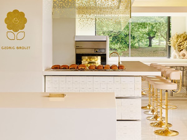 Elegant Cedric Grolet patisserie counter with pastries on display and golden stools.