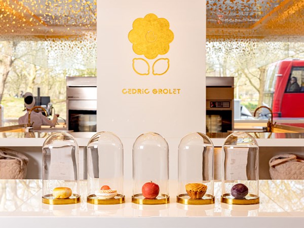 Five signature pastries under glass domes in a Cedric Grolet boutique interior.