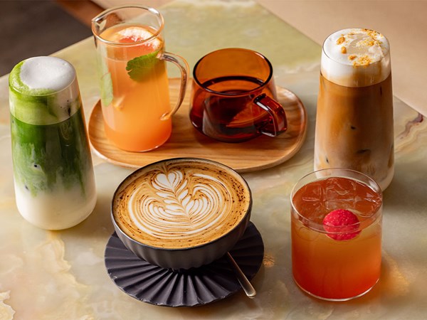 Assortment of colourful drinks including latte, iced coffee, matcha, and fruit infusions on a marble table.