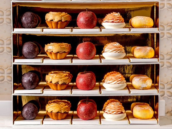 An elegant display of colourful pâtisserie, including fruit-shaped and intricately piped desserts, arranged in a gold-accented presentation box.