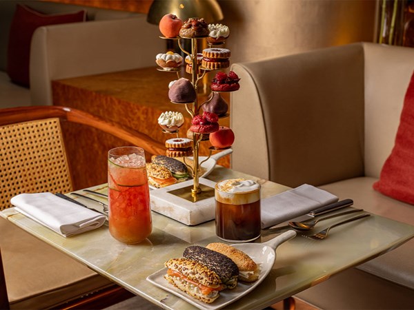 A marble table set with a towering stand of Cedric Grolet pastries, two savoury sandwiches, and iced and foamed drinks.