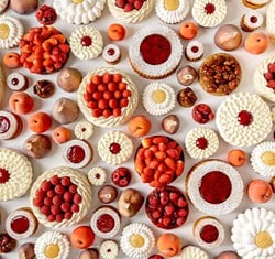 A neat row of daisy-like tartlets topped with white piped cream and vibrant yellow centres, resembling summer flowers on a white background.