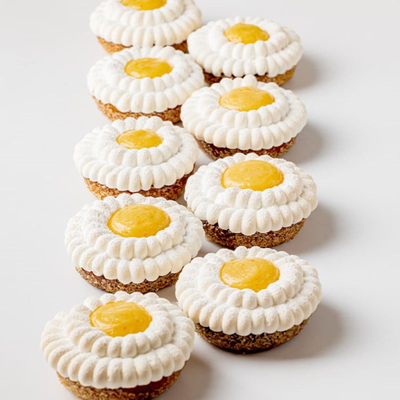 Realistic peach-shaped desserts with velvety skin arranged in a row, one halved to reveal juicy golden fruit filling inside.