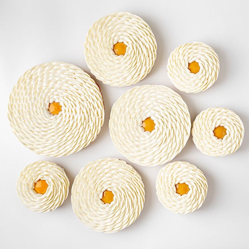 Multiple tarts with whipped cream piped in spirals and mango centres, displayed on a white background in varying sizes for visual harmony.