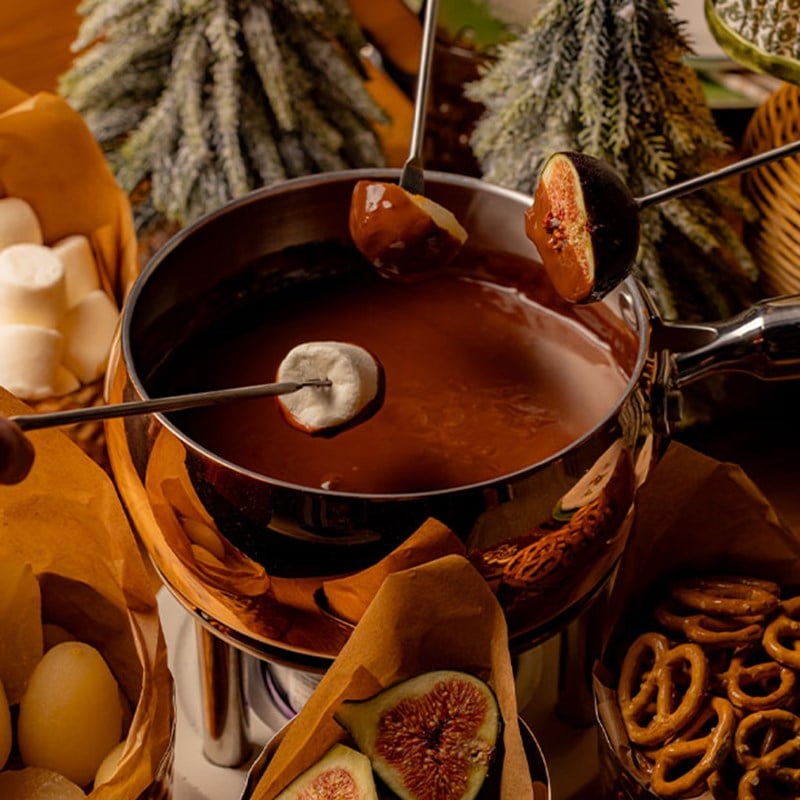 A luxurious chocolate fondue experience with fresh figs, marshmallows, and pretzels ready to be dipped into the velvety, rich chocolate, framed by snowy, festive decor.