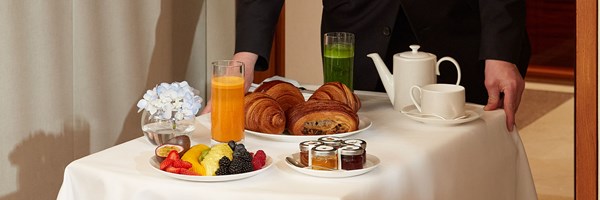 Room service breakfast setup with pastries, fresh fruit, juices, jams, tea set, and a small flower arrangement on white tablecloth.