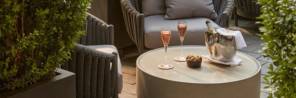 Leafy terrace setting at The Berkeley Bar with two glasses of rosé, a silver champagne bucket, and a bowl of olives on a round cream table.