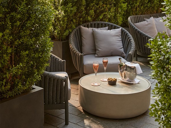 Wide shot of The Berkeley Bar’s terrace, showing lounge chairs, champagne on ice, and glasses of rosé surrounded by tall hedges and Mayfair architecture.