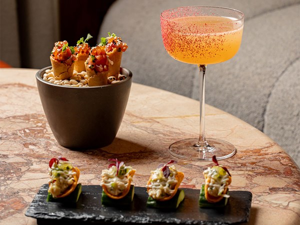 Close-up of summer small plates at The Berkeley Bar, featuring yellowtail tartare cones in a black bowl and lobster bites on cucumber with a citrus cocktail.