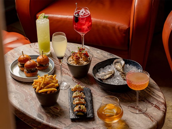 A marble table at The Berkeley Bar set with wagyu sliders, truffle fries, oysters on ice, yellowtail cones, mini lobster tacos, and five signature cocktails.