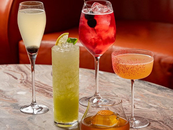 Selection of five vibrant summer cocktails on a marble table at The Berkeley Bar, including a red spritz, citrus highball, coupe with pink salt rim, and whisky serve.