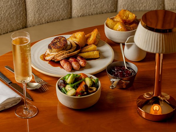Festive roast dinner with turkey, roast potatoes, vegetables and cranberry sauce served on a wooden table with a glass of fizz.