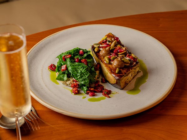 Plated main with roasted fish, wilted greens, seeds, and pomegranate, finished with green herb oil.