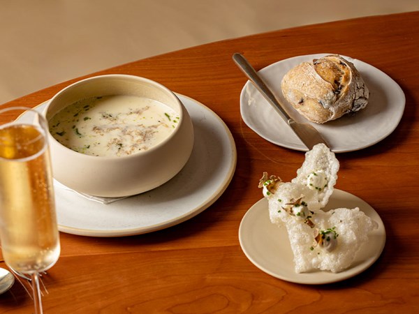 Creamy soup served with bread and crisp garnish on a wooden table, paired with a glass of sparkling wine.