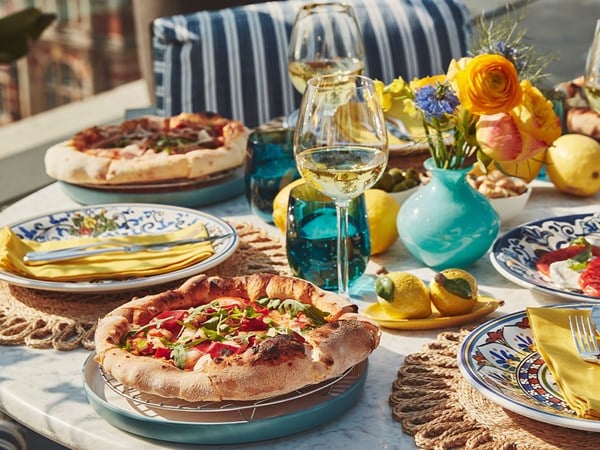 Outdoor table with fresh pizza, wine glasses, and vibrant floral decorations.