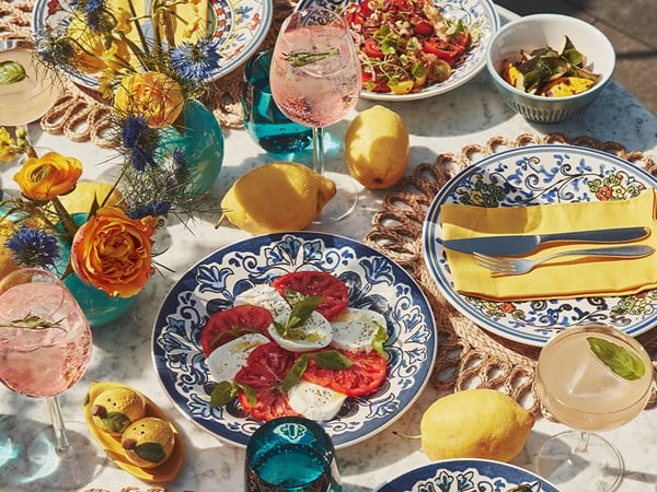Colourful summer table setting with caprese salad, cocktails, and bright flowers.