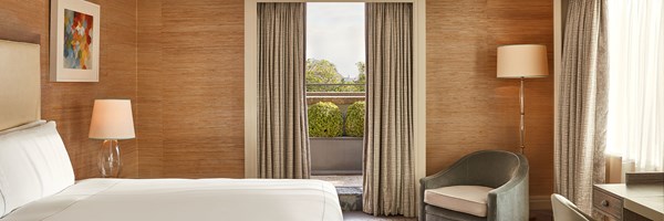 Spacious bedroom with neutral tones, large bed, and terrace access framed by curtains, offering views of lush greenery outside.