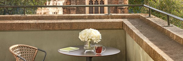 Private terrace with two woven chairs, round table, white hydrangeas, tea, and a notebook, overlooking a Gothic-style church.