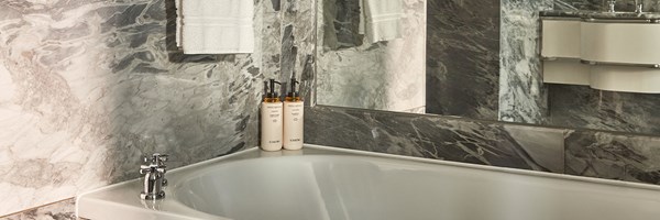 Marble bathroom with twin basins, large mirror, and premium toiletries on the counter, illuminated by soft natural and overhead light.