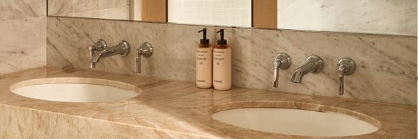 Polished marble bathroom with dual sinks, chrome fixtures, and matching body care products arranged by a large mirror.