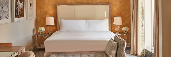 Bright hotel bedroom with a king-sized bed, two bedside tables with lamps, and a neutral palette of cream and beige