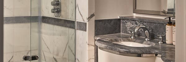 Marble bathroom with a walk-in glass shower, chrome fixtures, and a dark stone vanity with amenities.