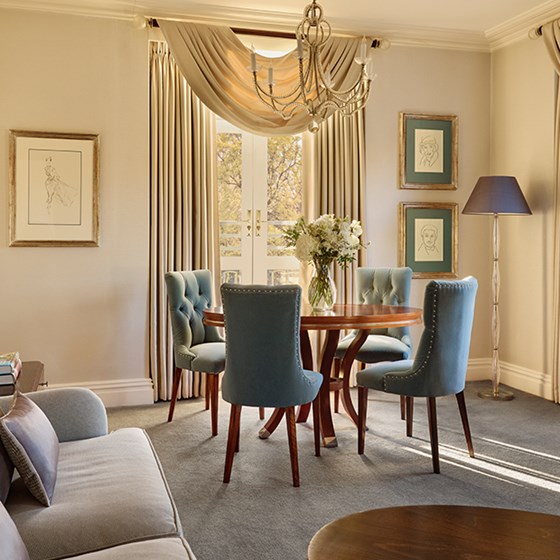 Round wooden dining table with four blue velvet chairs, a glass vase of white flowers in the centre, and framed sketches on the wall behind at The Berkeley.