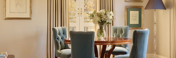 Round wooden dining table with four blue velvet chairs, a glass vase of white flowers in the centre, and framed sketches on the wall behind at The Berkeley.