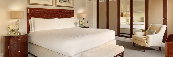 Elegant bedroom with a king-sized bed, mirrored wardrobes, cream armchair, and classic bedside lamps in The Berkeley Suite.