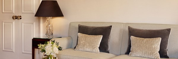 Neutral-toned sofa with grey and beige textured cushions beside a crystal lamp and white flower arrangement in The Berkeley Suite.