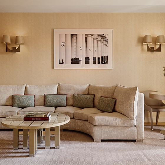 Neutral-toned living room with a curved upholstered sofa, patterned cushions, tiled coffee table with stacked books, and a framed black-and-white photograph of architectural columns on the wall.