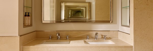 Modern bathroom with twin cream marble sinks, chrome taps, and an optical infinity mirror framed in chrome above the vanity.